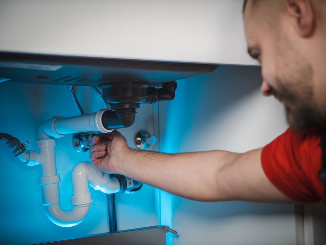 Plumber working on kitchen sink plumbing and pipe fittings, used as a hero graphic for local trade business websites.